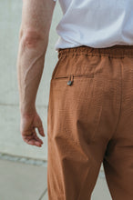 Laden Sie das Bild in den Galerie-Viewer, Detail of the elasticated waistband on rust terracotta trousers