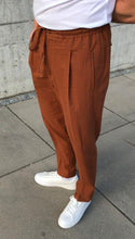 Laden Sie das Bild in den Galerie-Viewer, Full length shot of model wearing rust seersucker trousers in a summer setting